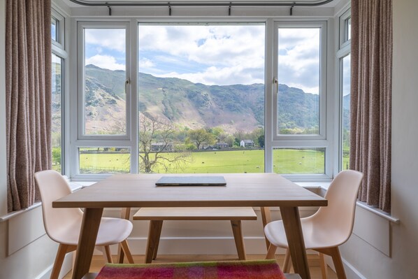 A dining area with a table and chairs, large windows with a view of a green valley and mountains.