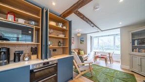 Une cuisine moderne avec des étagères en bois, un four encastré et un coin repas agrémenté d’un tapis vert.