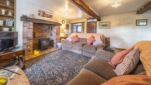 A cozy living room with a brick fireplace, a sofa set, a wooden table, and a patterned rug. - Drawell Cottage -  Cottage on a working farm with splendid views (Sedbergh)