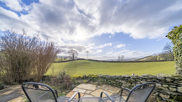 A patio with two metal chairs and a table, overlooking a green field and stone wall, under a partly cloudy sky. - Drawell Cottage -  Cottage on a working farm with splendid views (Sedbergh)