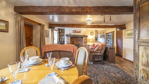 A dining area with a wooden table set for four, surrounded by chairs. A brick fireplace is visible in the background, and the room has exposed wooden beams on the ceiling. - Drawell Cottage -  Cottage on a working farm with splendid views (Sedbergh)
