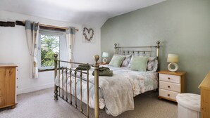Un dormitorio con cama con dosel, cómoda de madera, mesita de noche con lámpara y ventana con cortinas.