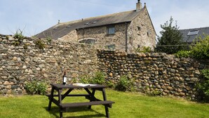 Una casa de piedra con un muro de piedra y una mesa de picnic de madera al frente.