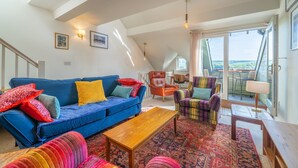 A spacious living room with a blue sofa, colorful armchairs, a wooden coffee table, and a large window offering a view of the outdoors. - Bowling Fell Cottage -  Kendal Townhouse with Views (Kendal)