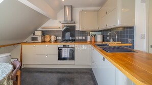 A modern kitchen with white cabinets, a wooden countertop, a built-in oven, and a stainless steel range hood. - Bowling Fell Cottage -  Kendal Townhouse with Views (Kendal)