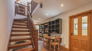 Un escalier en bois mène à une pièce où se trouvent une bibliothèque, une table et des chaises.