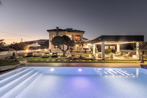 Une maison moderne dotée d’une piscine, d’un espace extérieur aménagé pour se détendre et d’un patio bien éclairé.