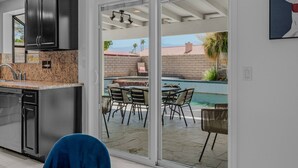 A modern kitchen with granite countertops, stainless steel appliances, and a sliding glass door leading to an outdoor patio with a pool and dining area. - Vibrant Home & Sparkling Pool. Entertain in Luxury at this Desert Gem! #75-354 (Bermuda Dunes)