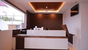 A modern reception desk with a wooden finish, a ceiling fan, and a mounted TV. - Hotel Sahaya Arasi (Kanyakumari)