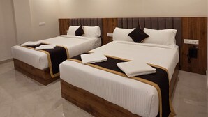 A hotel room with two beds, wooden headboards, white bedding, and a ceiling fan. - Hotel Sahaya Arasi (Kanyakumari)