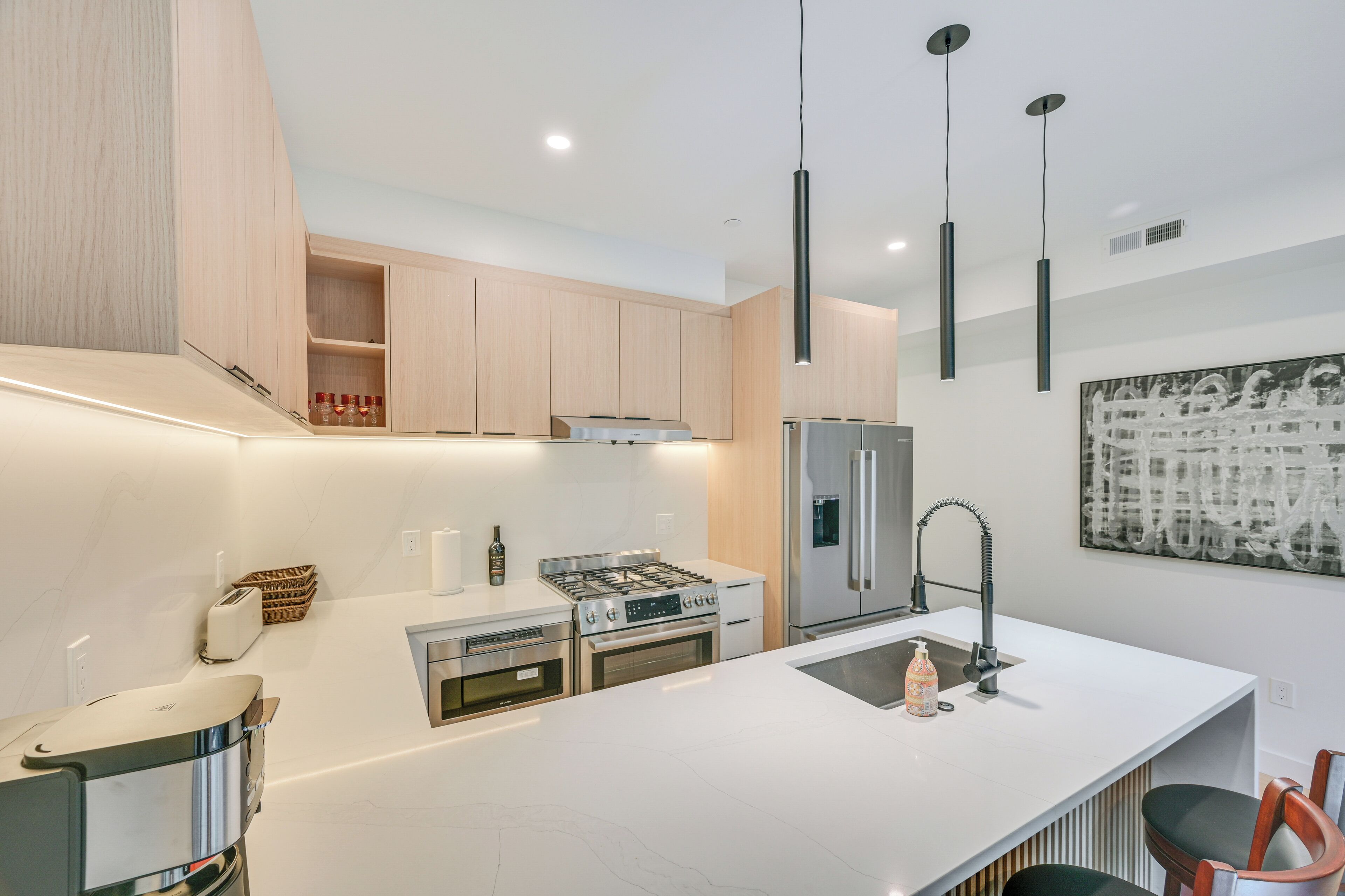 Une cuisine moderne dotée d’un îlot central, d’appareils électroménagers en acier inoxydable, de meubles en bois et de luminaires suspendus.