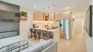 A modern kitchen with a central island, bar stools, a refrigerator, and pendant lighting.