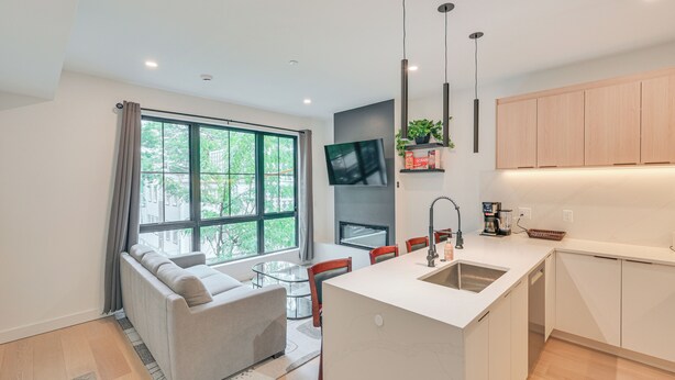 A modern kitchen with a central island, a dining area with a glass table, and a sofa.