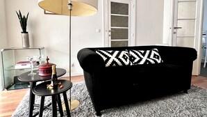 A living room with a black sofa, a round table with a lamp, a potted plant, and a door in the background. - Chic & Green (Brussels)