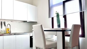 A modern kitchen with white cabinets, a stainless steel sink, and a window with a view of the outdoors. There are two white chairs at a small table. - Chic & Green (Brussels)