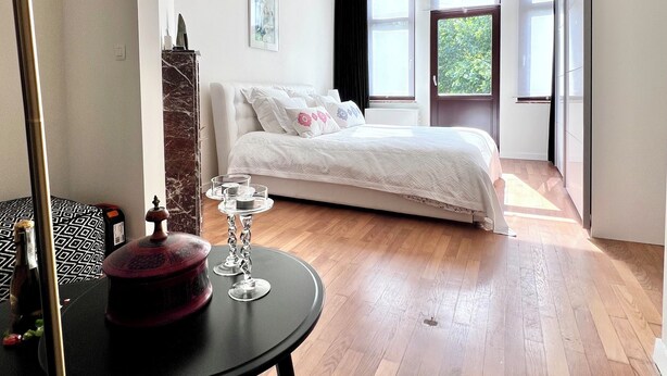 A modern bedroom with a bed, a chandelier, a window, and a wooden floor. - Chic & Green (Brussels)