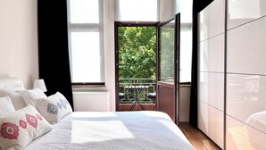A bedroom with a large bed, a wardrobe, and a balcony with a view of greenery. - Chic & Green (Brussels)