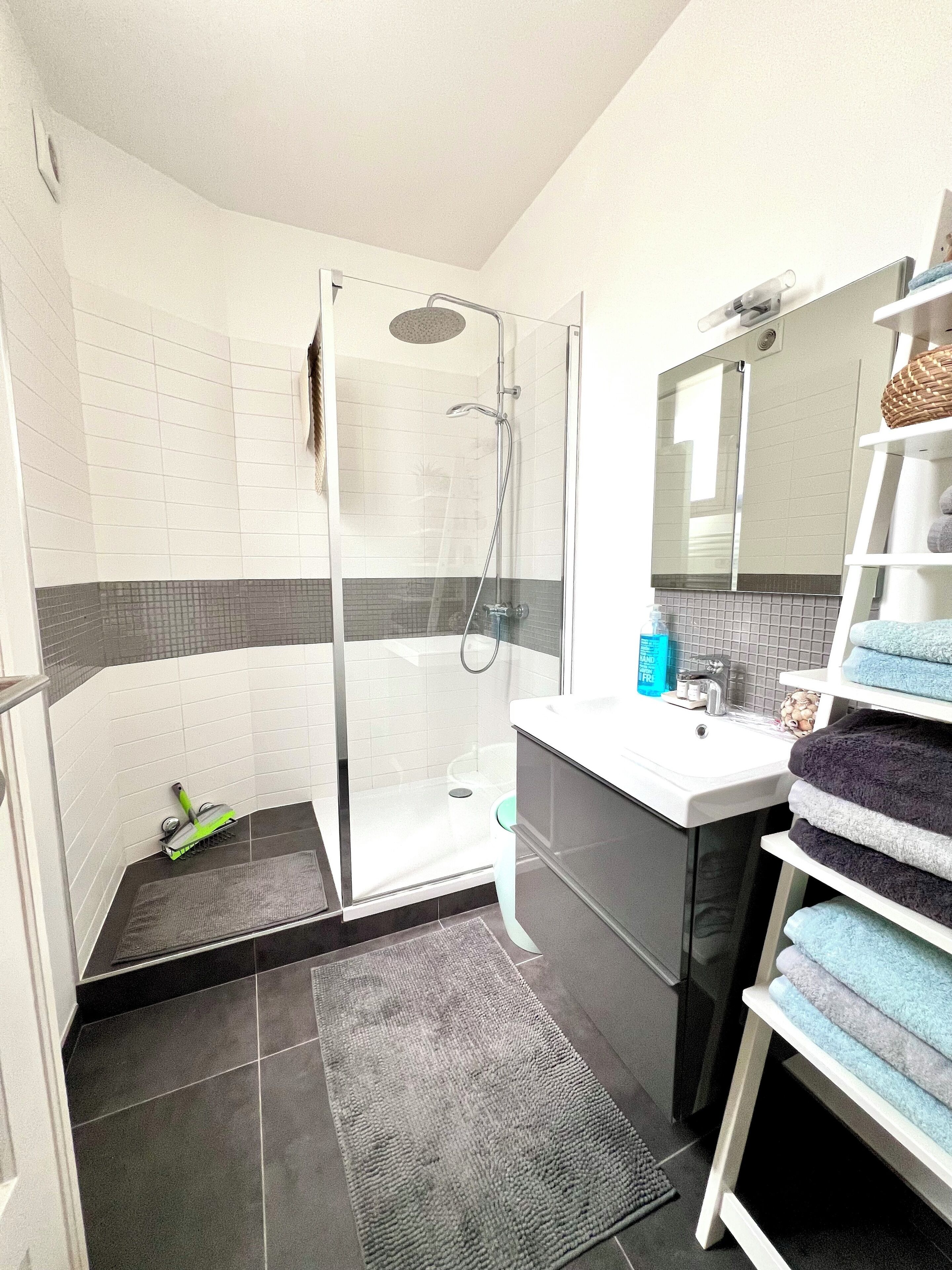 Une salle de bain moderne avec une douche à parois de verre, un lavabo blanc avec un miroir au-dessus et un porte-serviettes avec des serviettes pliées.