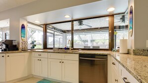 A modern kitchen with white cabinets, granite countertops, a dishwasher, and a large window with a view of the outdoors. - Private Pool & Yard: Family Home in Port St Lucie (Port St. Lucie)