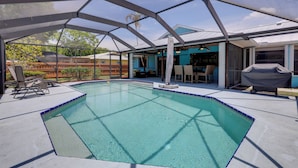 A covered swimming pool with a clear blue water, surrounded by a metal frame structure, and equipped with lounge chairs and a barbecue area. - Private Pool & Yard: Family Home in Port St Lucie (Port St. Lucie)