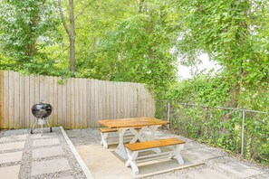 Un patio exterior con mesa y banco de madera, una parrilla y valla de madera.