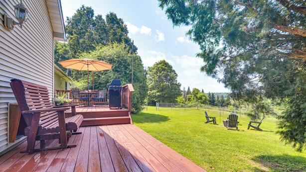 A wooden deck with outdoor furniture, a patio umbrella, and a view of a grassy yard with trees. - Family Getaway w/ Deck: 3 Mi to Lake Champlain (Colchester)