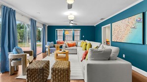 A modern living room with a white sofa, a coffee table, and a large window with blue curtains. - Sleeps 20~Heated Pool~Pickleball~Hot Tub~Fire Pit (Largo)