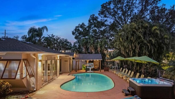 A swimming pool with lounge chairs and a hot tub, surrounded by trees and a building with large windows. - Sleeps 20~Heated Pool~Pickleball~Hot Tub~Fire Pit (Largo)