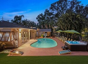 Une piscine dotée de chaises longues et d’un jacuzzi, entourée d’arbres et bordée d’un bâtiment aux grandes fenêtres.