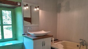 Een badkamer met een witte wastafel, een bad en een raam met uitzicht op groen.