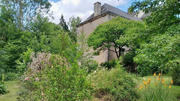 Een stenen gebouw omringd door weelderige begroeiing en bloeiende planten.
