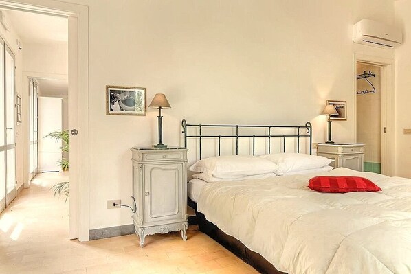 A bedroom with a bed, bedside tables, a lamp, a picture on the wall, and an air conditioner.