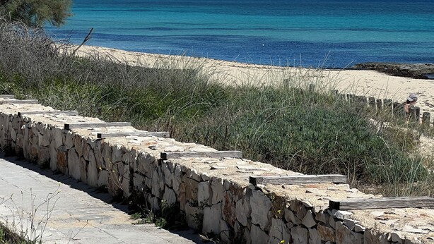 A coastal view with a stone wall, clear blue sky, and turquoise sea.