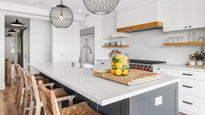 A modern kitchen with a large island, white cabinetry, and a hanging light fixture. - 3BR + Loft Ocean View | Rooftop, Hot Tub, Parking (Newport Beach)
