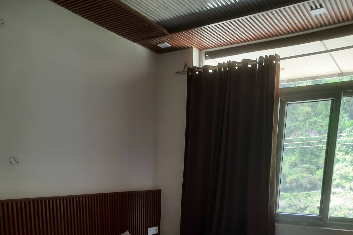 A hotel room with two beds, wooden headboards, a window with curtains, and a view of greenery outside.