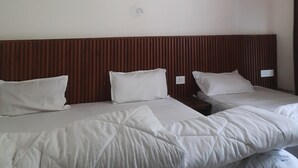 A hotel room with a wooden headboard, two beds with white bedding, a ceiling fan, and a plain white wall. - Hotel RRR (Jakholi)