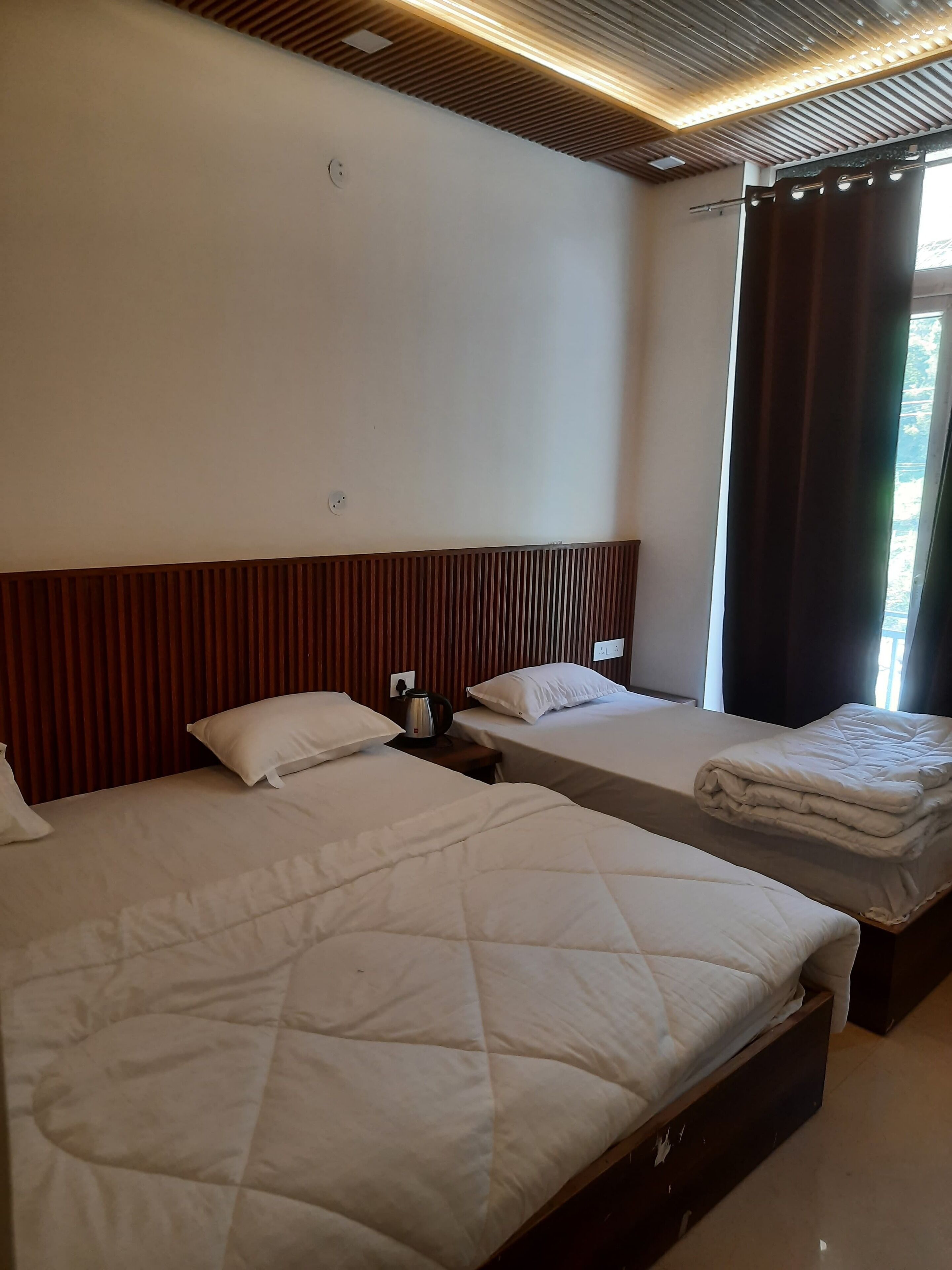 A hotel room with two beds, wooden headboards, a window with curtains, and a ceiling with recessed lighting.