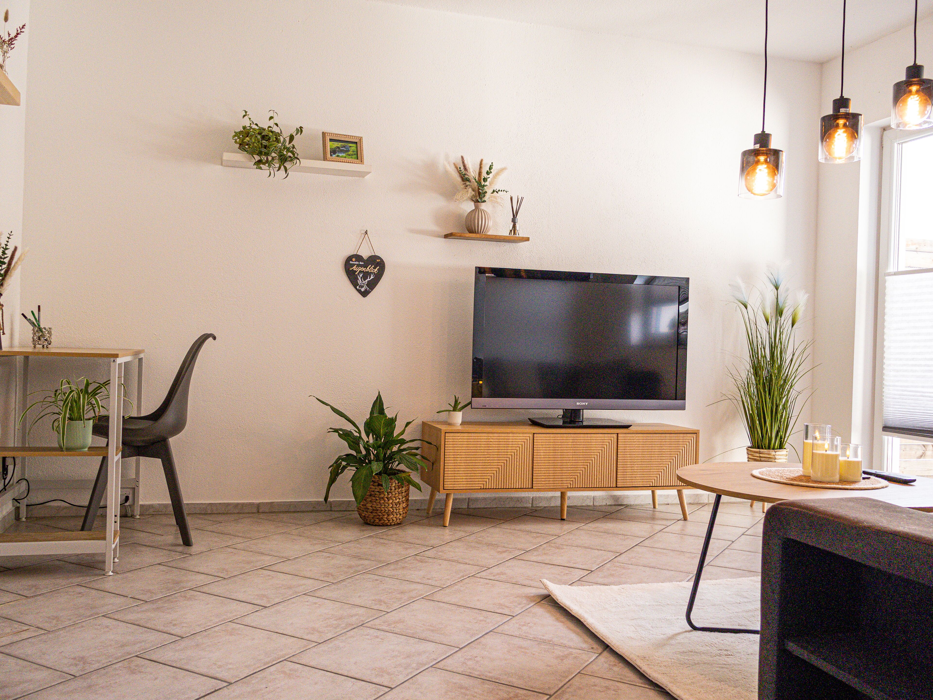 Een woonkamer met een flatscreen televisie op een houten kast, een eettafel met stoelen en verschillende potplanten.