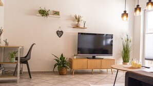 A living room with a flat-screen TV on a wooden cabinet, a dining table with chairs, and various potted plants. - Vacation apartment Allgäuherz Relax on lovingly furnished 55 sqm (Unknown)