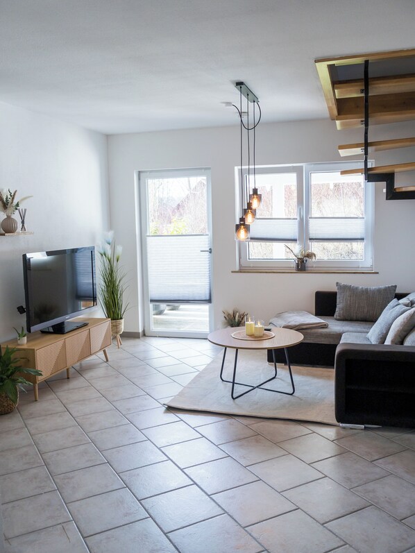 Ein modernes Wohnzimmer mit Flachbildfernseher, einer Couch, einem Couchtisch und einem Essbereich mit einem kleinen Tisch und Stühlen.