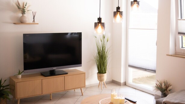 A modern living room with a flat-screen TV, wooden console, round coffee table, and hanging pendant lights. - Vacation apartment Allgäuherz Relax on lovingly furnished 55 sqm (Unknown)