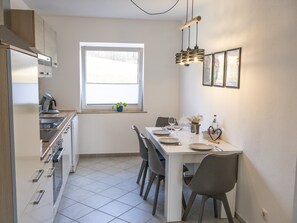 A modern kitchen with a dining area, featuring a window, a hanging light fixture, and a tiled floor. - Vacation apartment Allgäuherz Relax on lovingly furnished 55 sqm (Unknown)