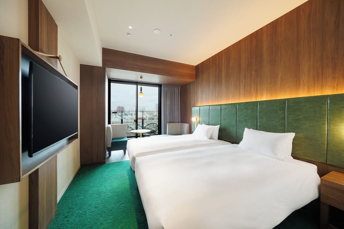 A hotel room with two beds, a TV, a balcony with a view, and a green carpet.