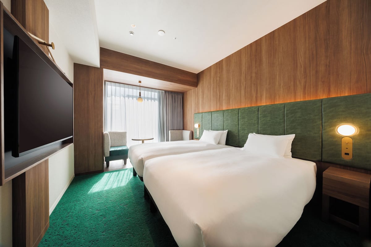 A hotel room with two beds, a flat-screen TV, a small table, and a chair.