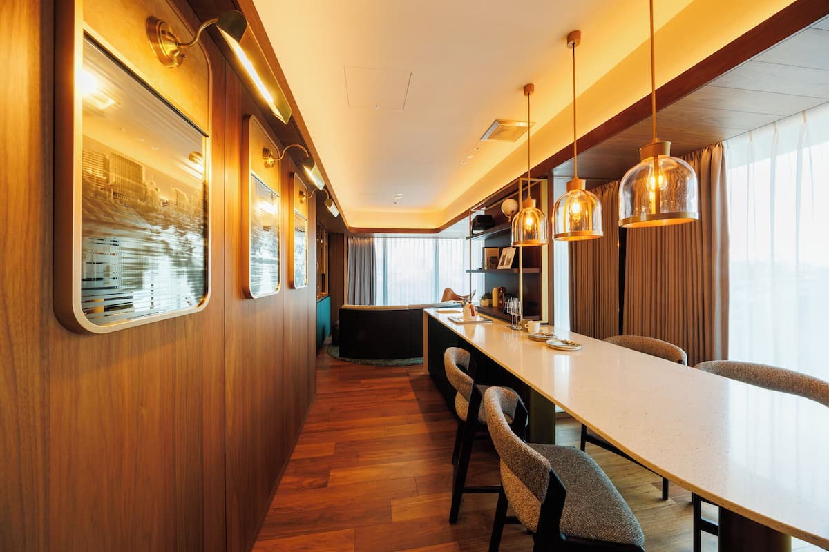 A modern kitchen with wooden cabinetry, a long countertop, and pendant lighting.