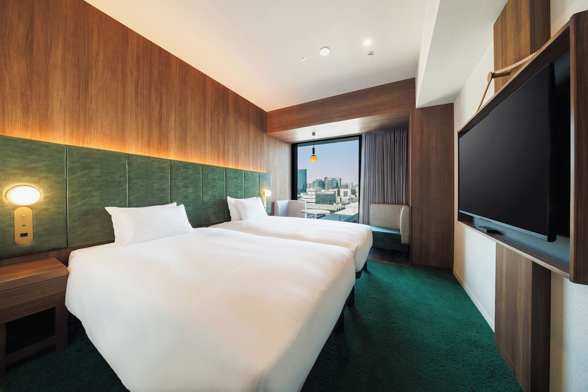 A hotel room with two beds, a large TV, a city view, and a green carpet.