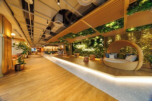A modern interior with a wooden reception desk, a seating area with cushions, and a wall adorned with greenery.