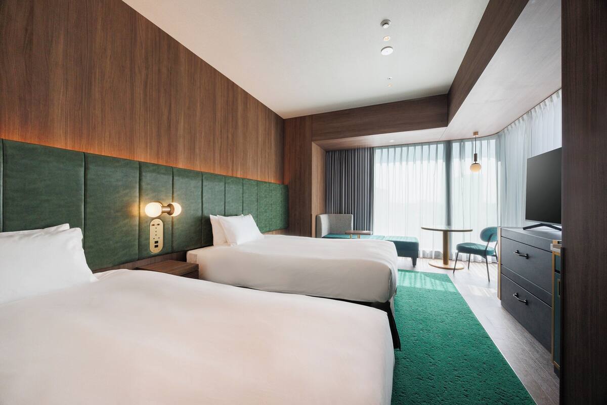 A hotel room with two beds, a desk, a chair, and a TV.