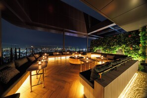 A rooftop bar with a city view, wooden flooring, and modern furniture.