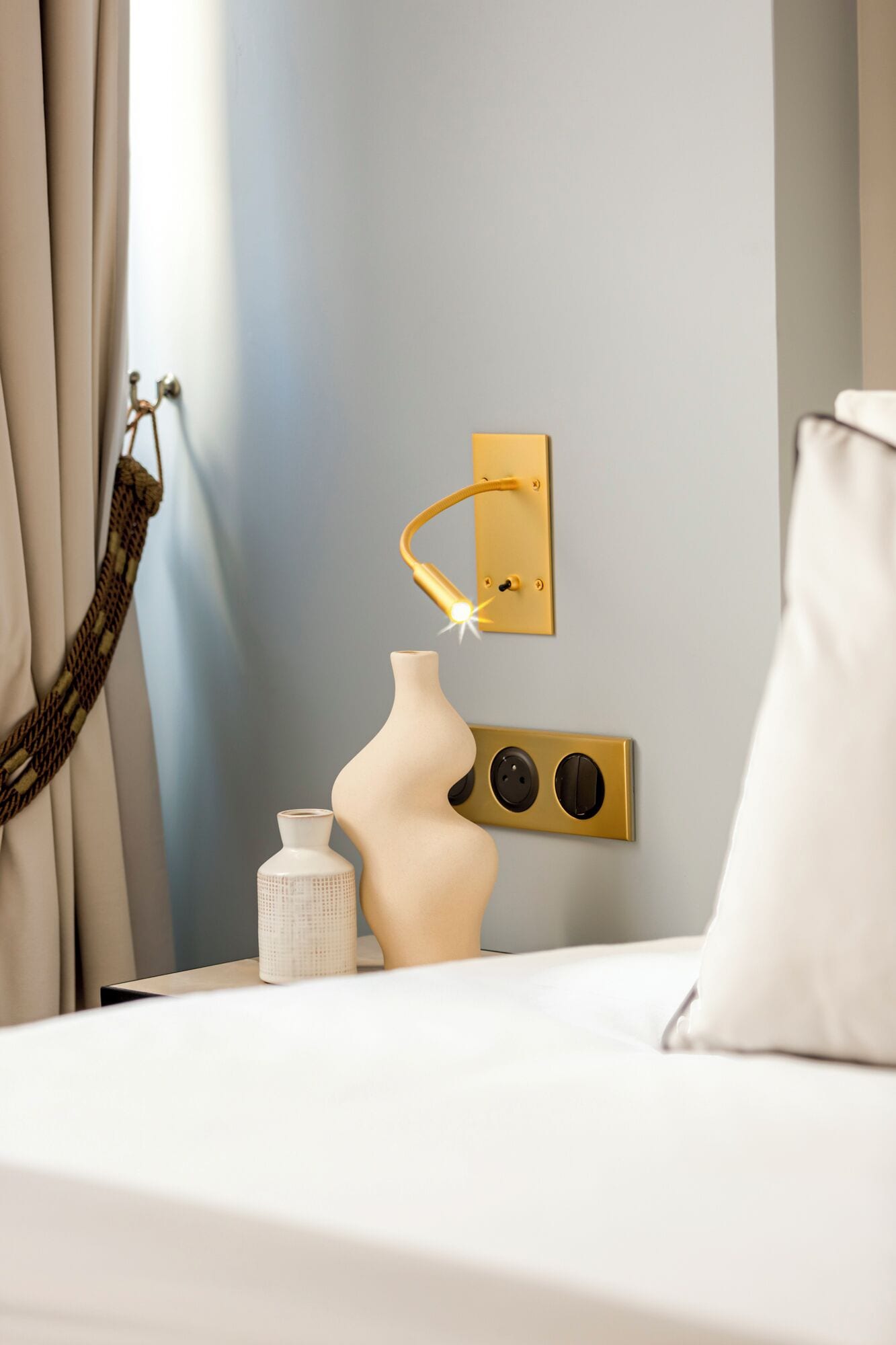 Een moderne slaapkamer met een bed, een wandlamp, een vaas en een hangstoel.